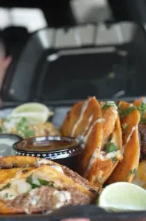 Tacos and enchiladas with lime wedges and salsa on a tray in a food truck window