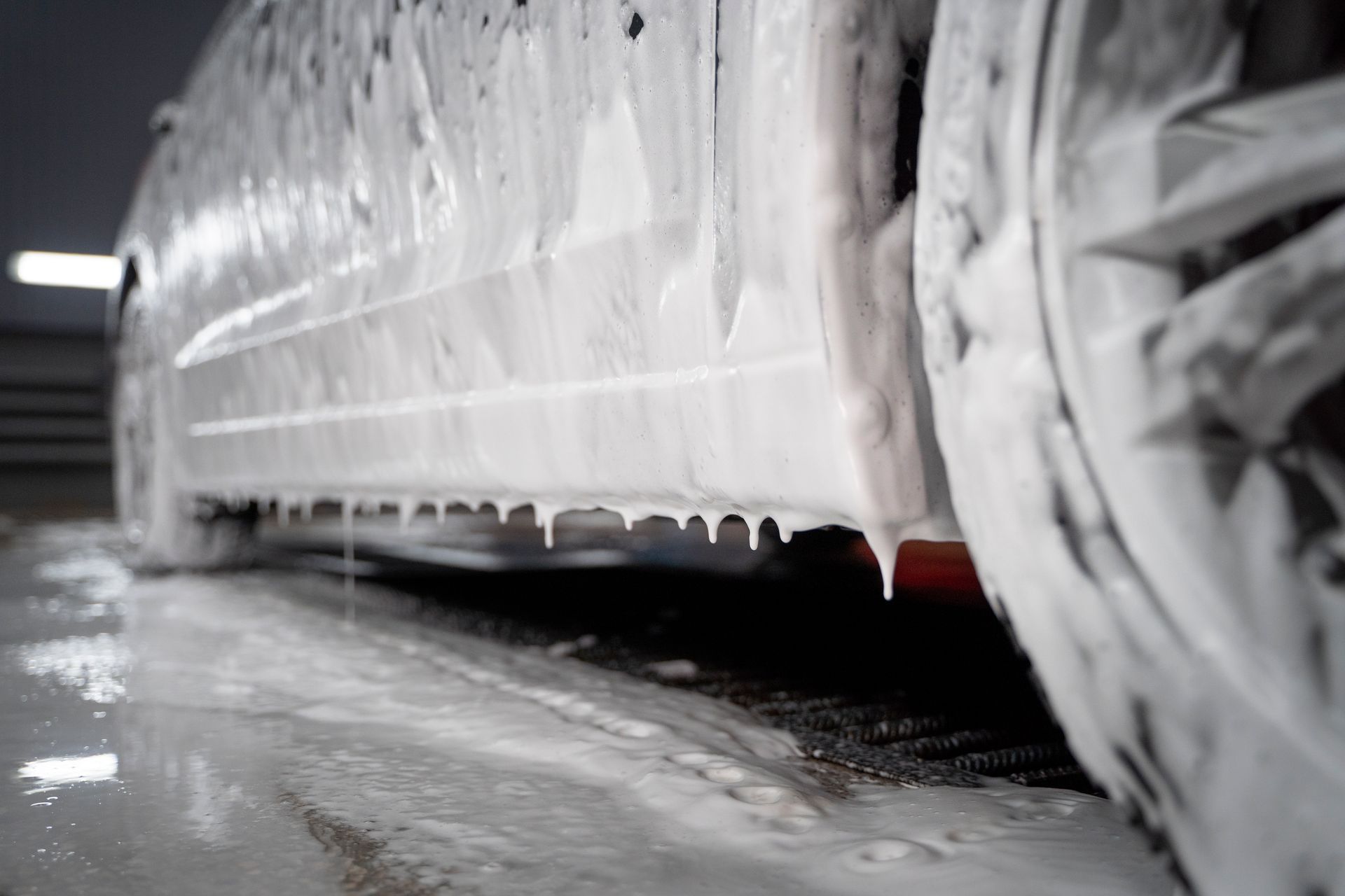 A close-up of a car's side covered in thick, white cleaning foam in a car wash bay.