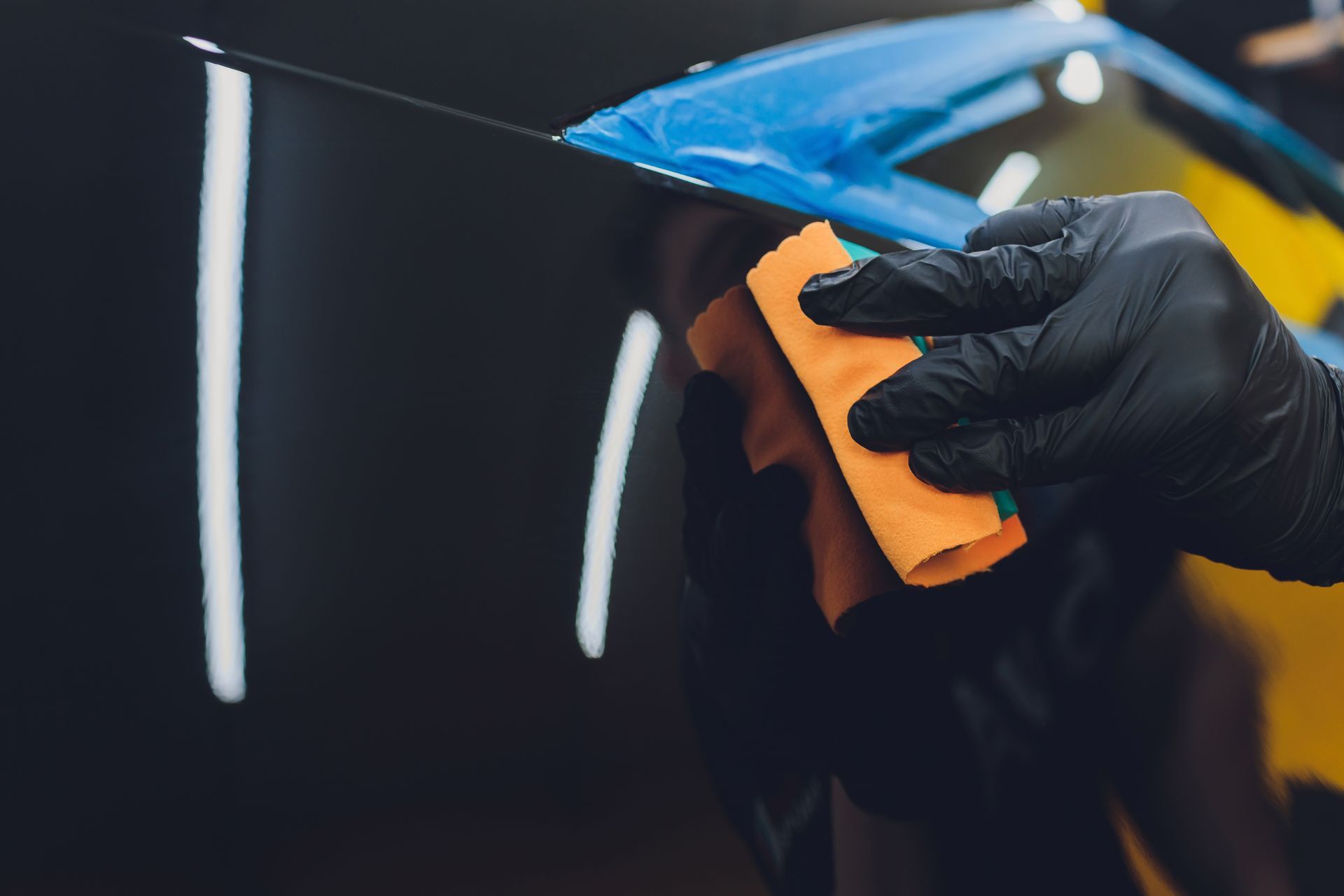 A pair of hands applies a clear paint protection film to the red rear quarter panel and taillight of a sports car.