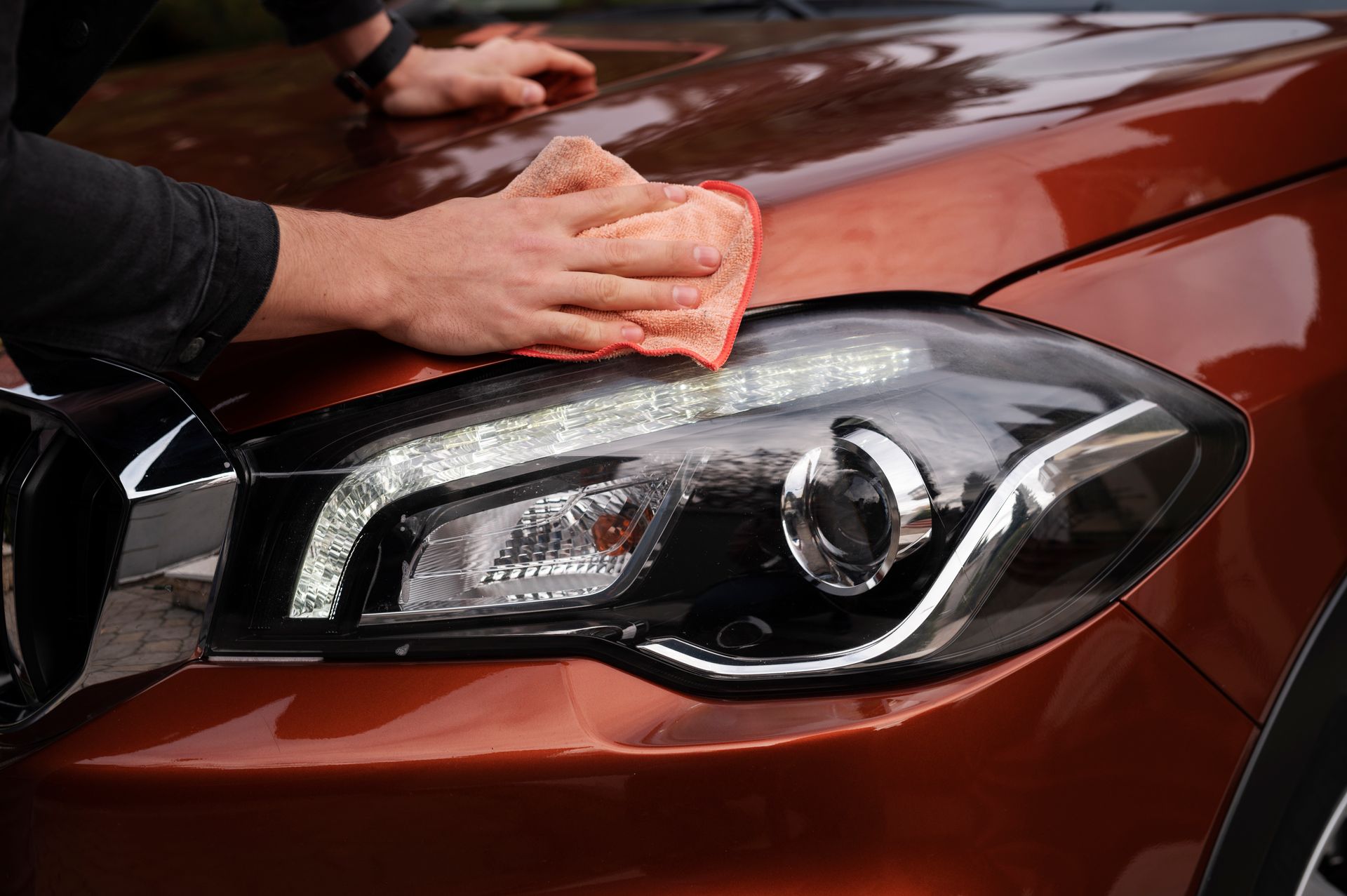 Hands applying a transparent protective film with soapy water onto the hood of a black car.