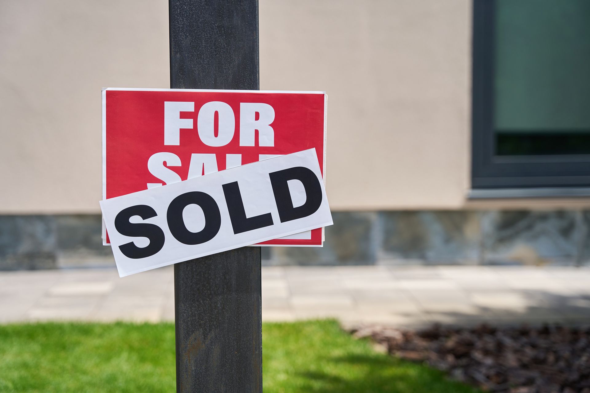 A for sale sign is sitting on a pole in front of a house.