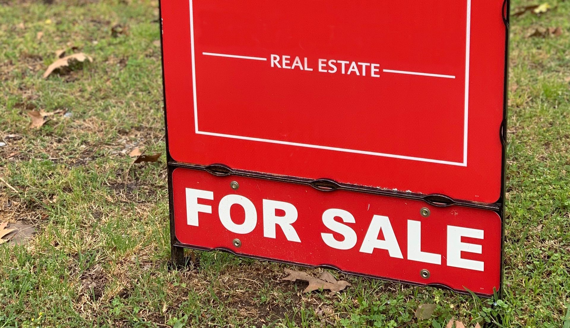A red for sale sign is sitting in the grass.