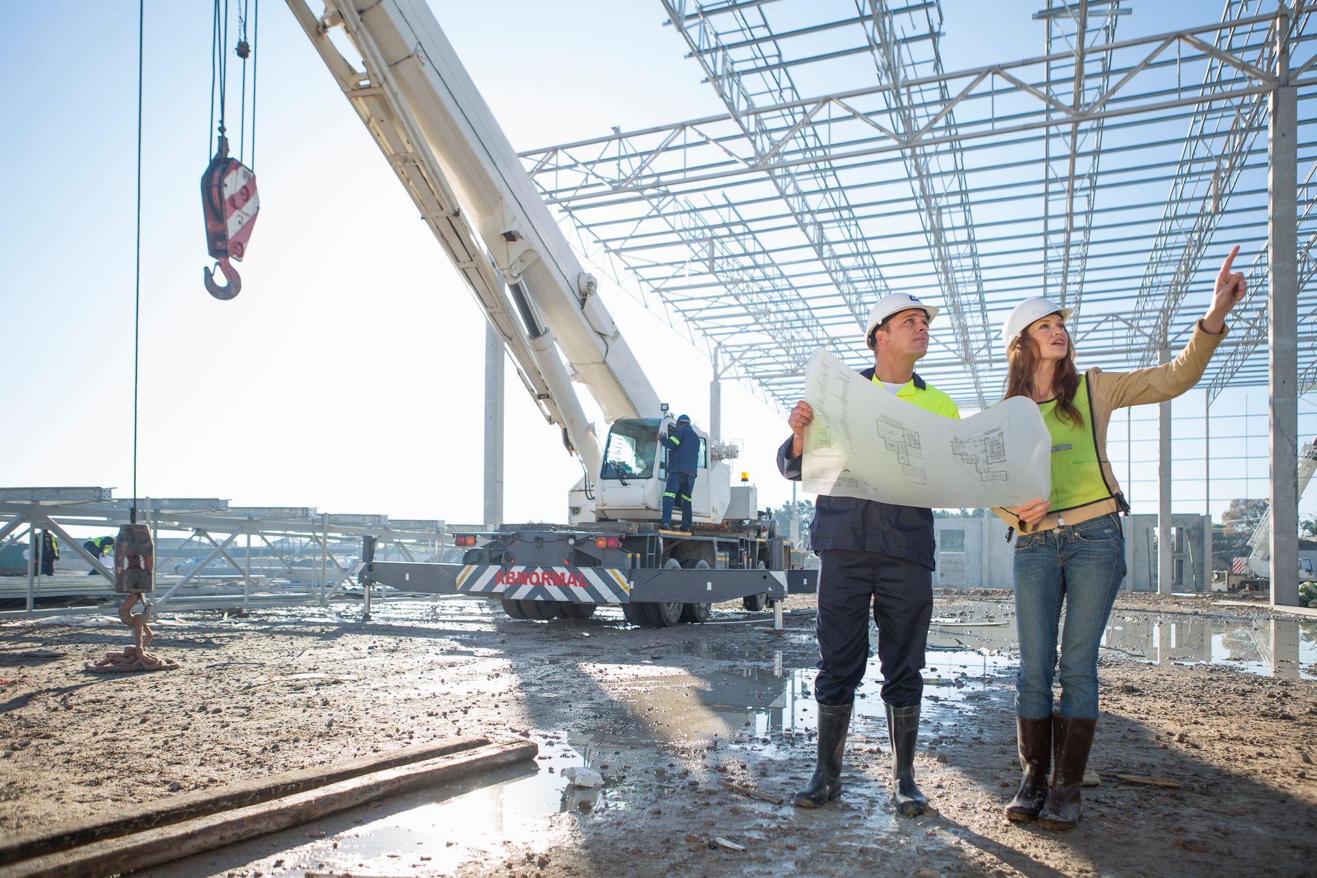 A man and a woman are standing on a construction site looking at a blueprint.
