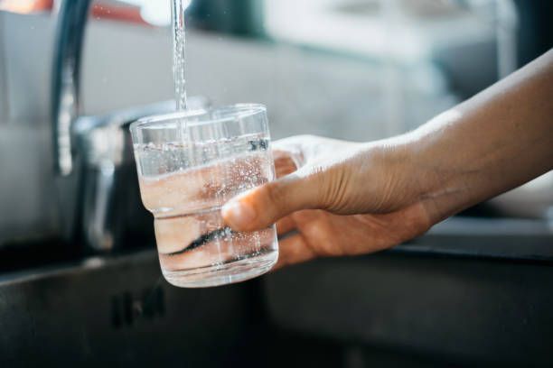 Close-up of a woman's hand filling a glass of filtered water from the tap in a kitchen sink at home.
