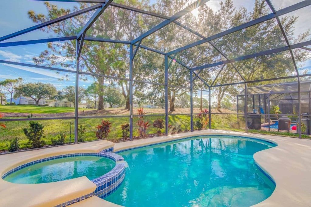 A large swimming pool is surrounded by a screened in area.