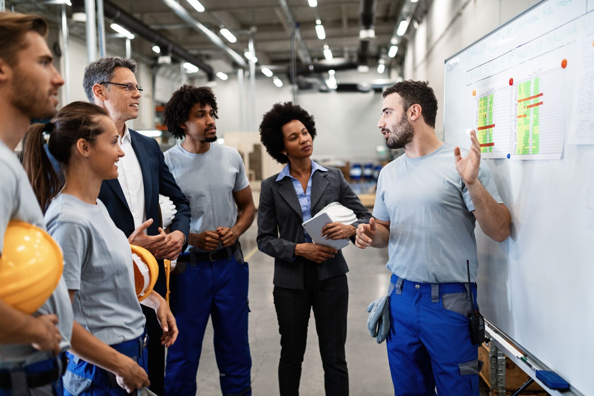 A group of people are standing around a whiteboard in a factory.