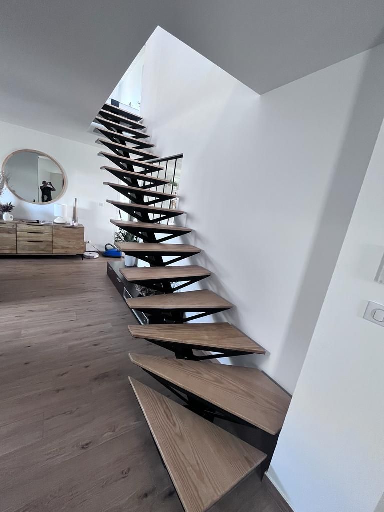 Un escalier flottant moderne avec des marches en bois et des supports en métal noir, à l'intérieur d'une maison lumineuse et contemporaine.