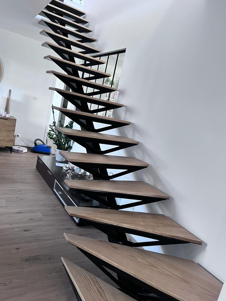 Un escalier flottant moderne, avec des marches en bois clair et une structure en métal noir, monte le long d'un mur blanc dans un salon.