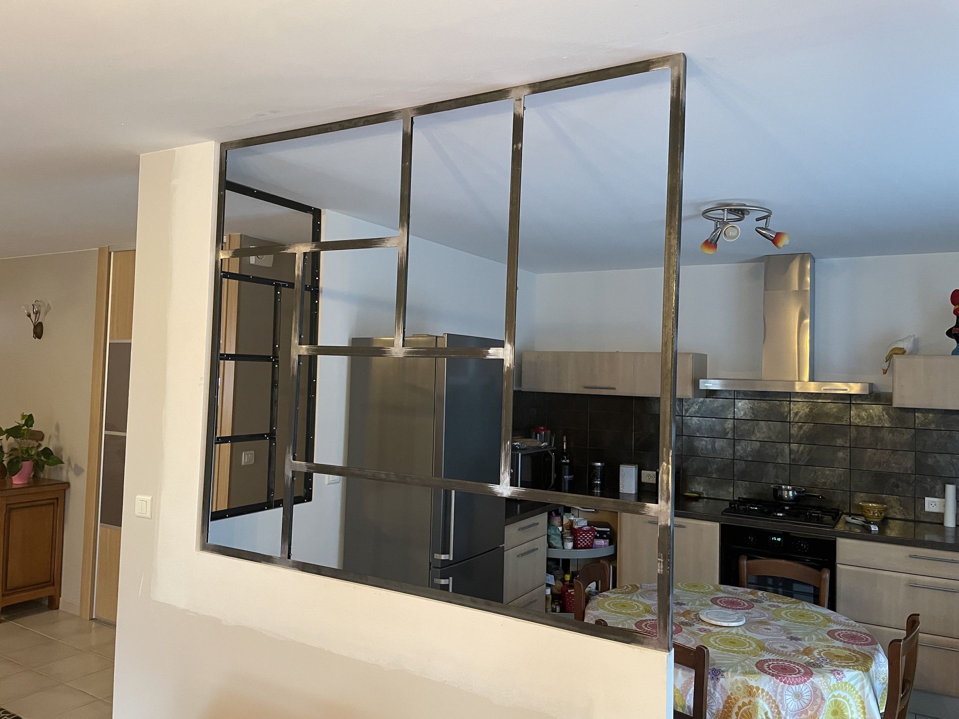 Une cloison en métal noir est fixée à mi-hauteur d'un muret, séparant ainsi l'espace cuisine de l'espace salon.