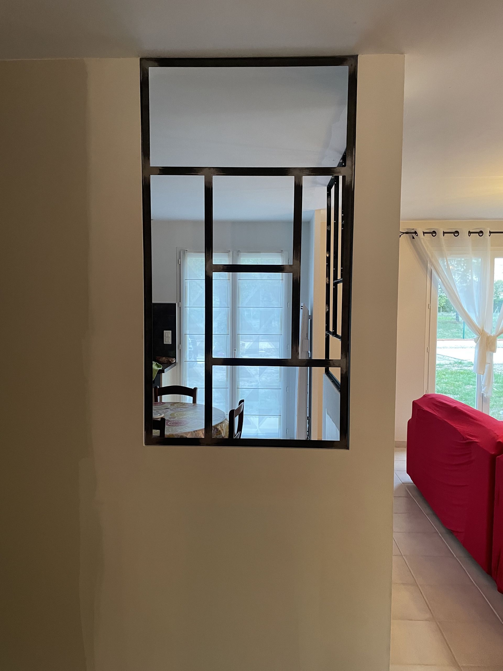 Un mur intérieur est doté d'une cloison en métal noir avec des panneaux de verre rectangulaires, dévoilant une salle à manger.