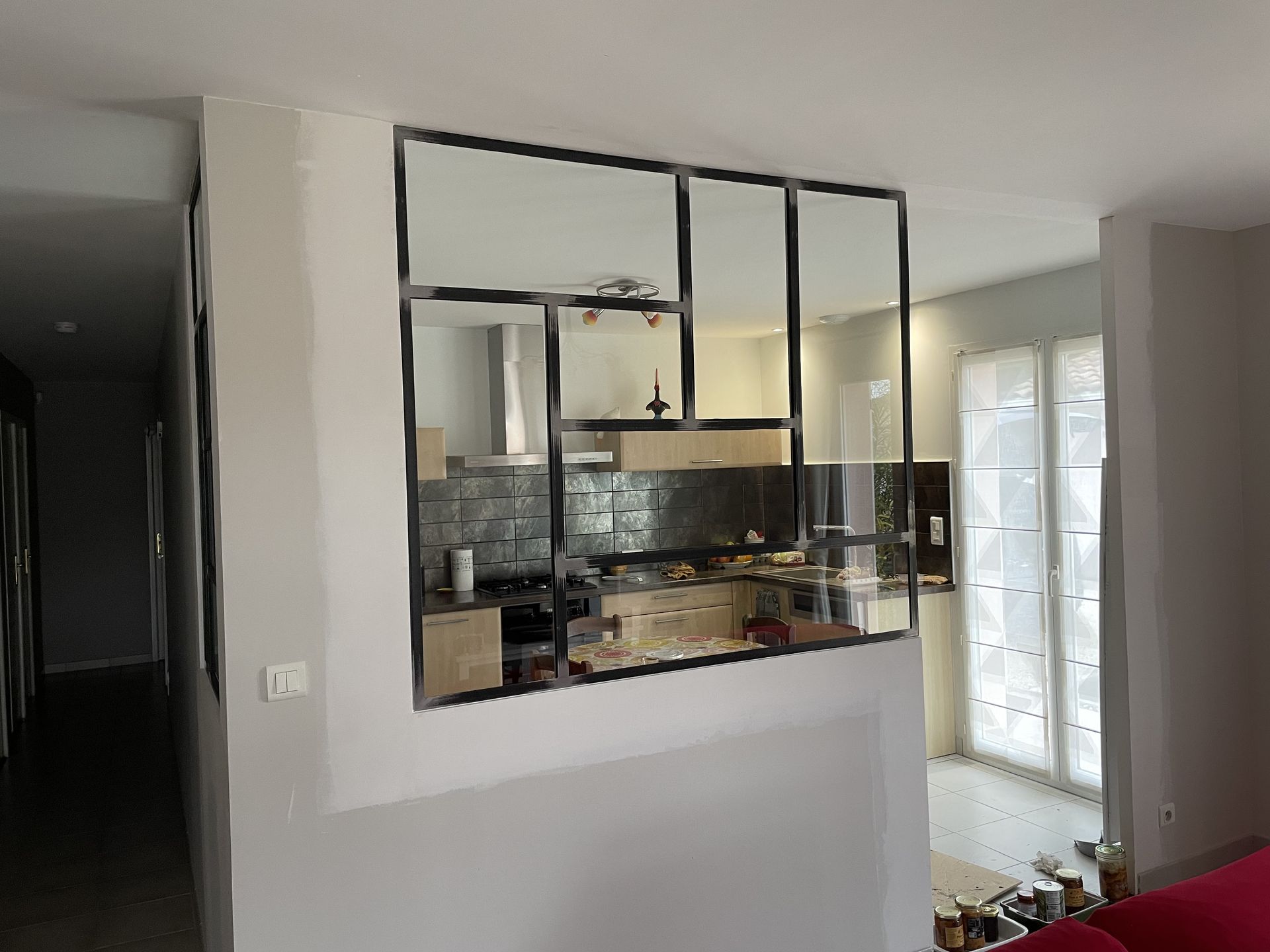 Dans un intérieur moderne, une cloison vitrée à ossature métallique sépare la cuisine du salon.