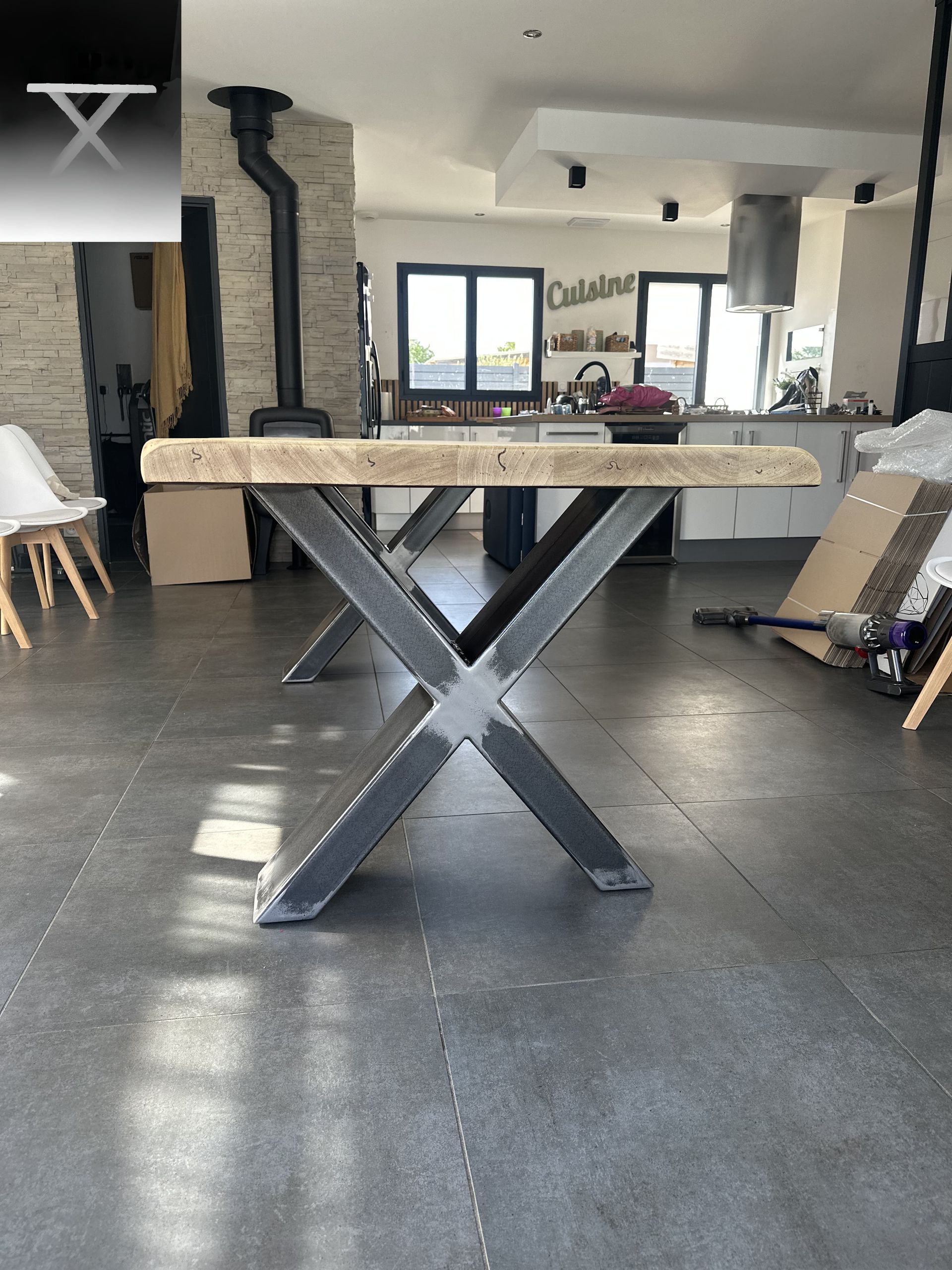 Une table à manger rustique en bois avec un piètement en métal foncé en forme de X dans une cuisine moderne et lumineuse.