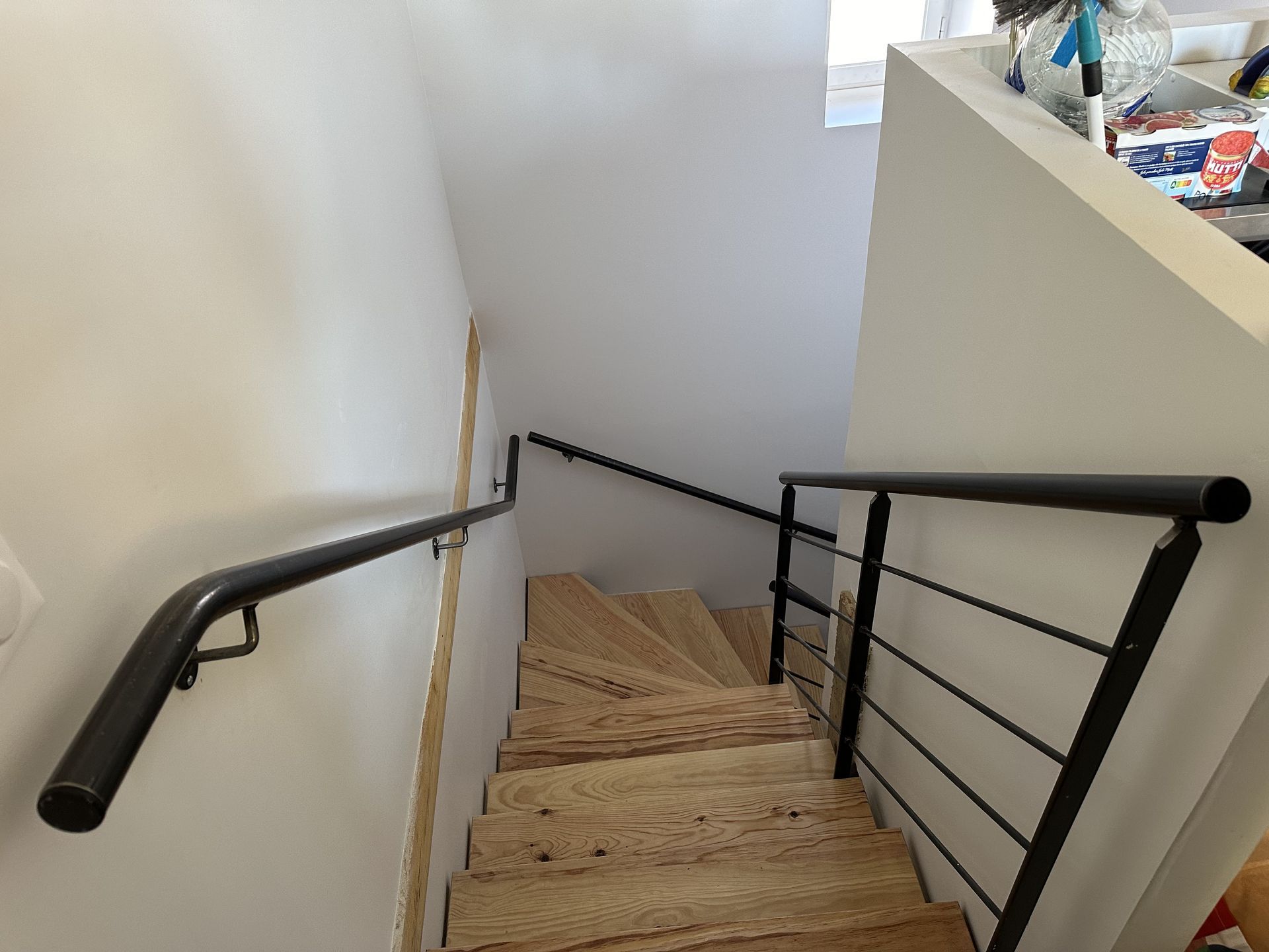 Vue de dessus d'un escalier en bois présentant une rampe noire sur le mur de gauche et une rambarde en métal noir sur le mur de droite.