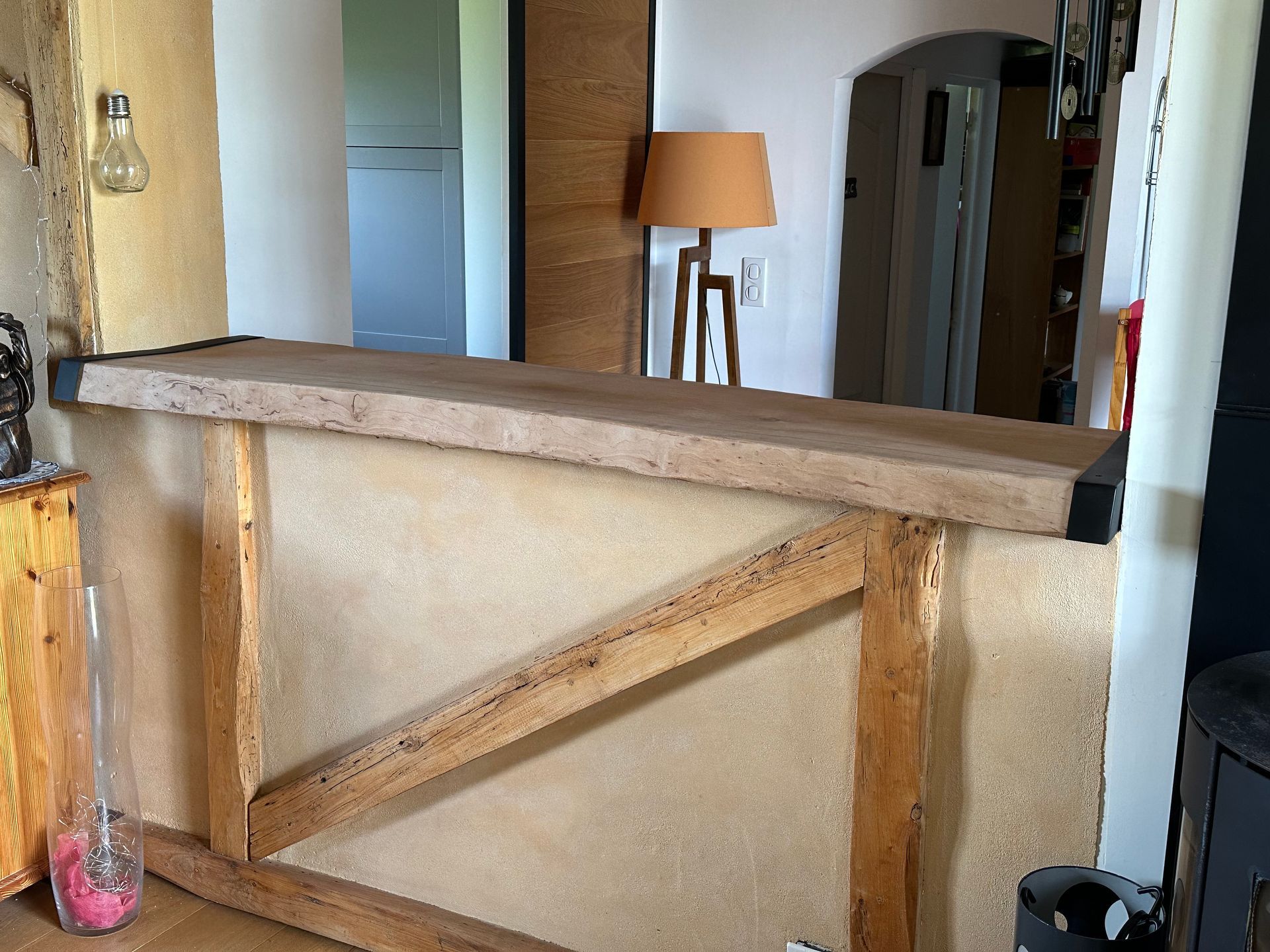 Un comptoir de bar rustique en bois, avec un mur en plâtre beige texturé et une structure en bois, dans un intérieur de maison.