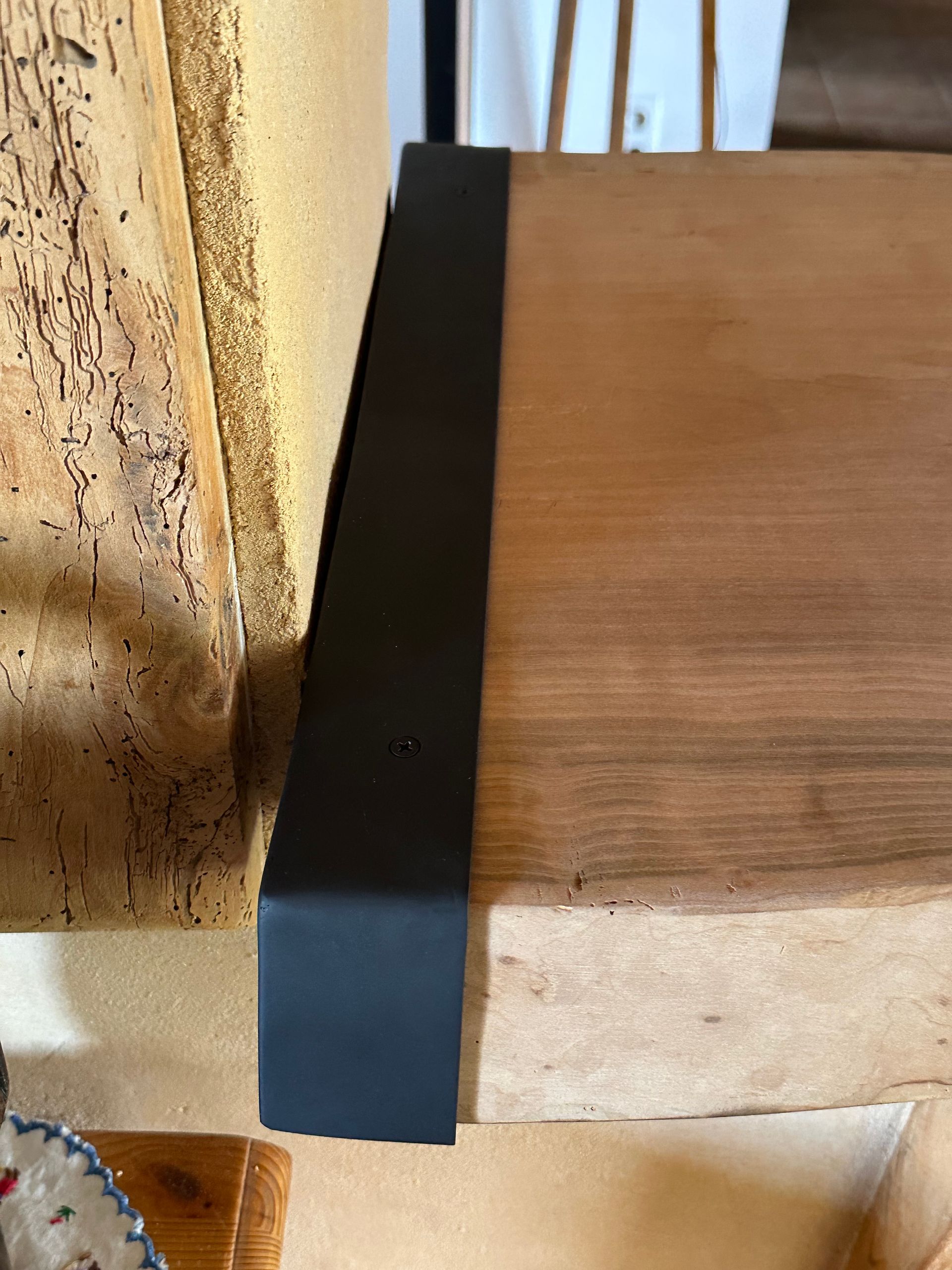 Un support métallique noir mat fixé sur le bord supérieur et latéral d'une cheminée en bois brut de couleur claire.