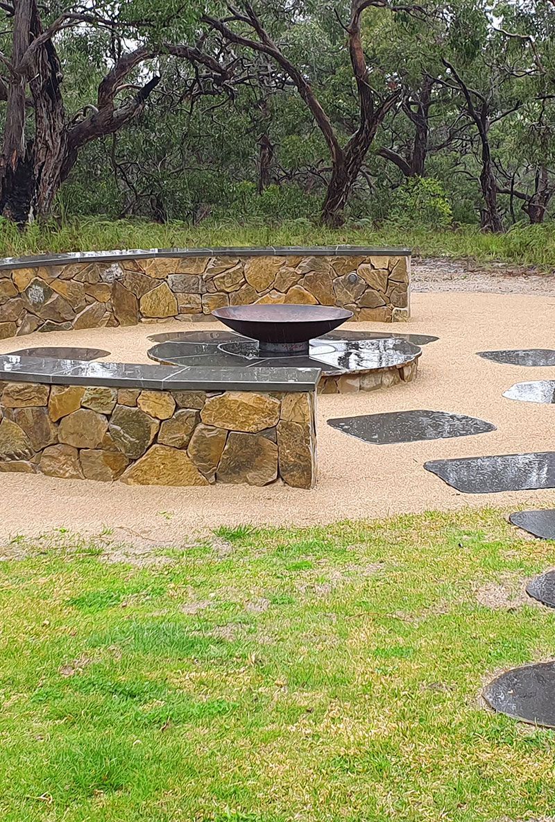 Stone fire pit with surrounding seating area in a wooded park setting.