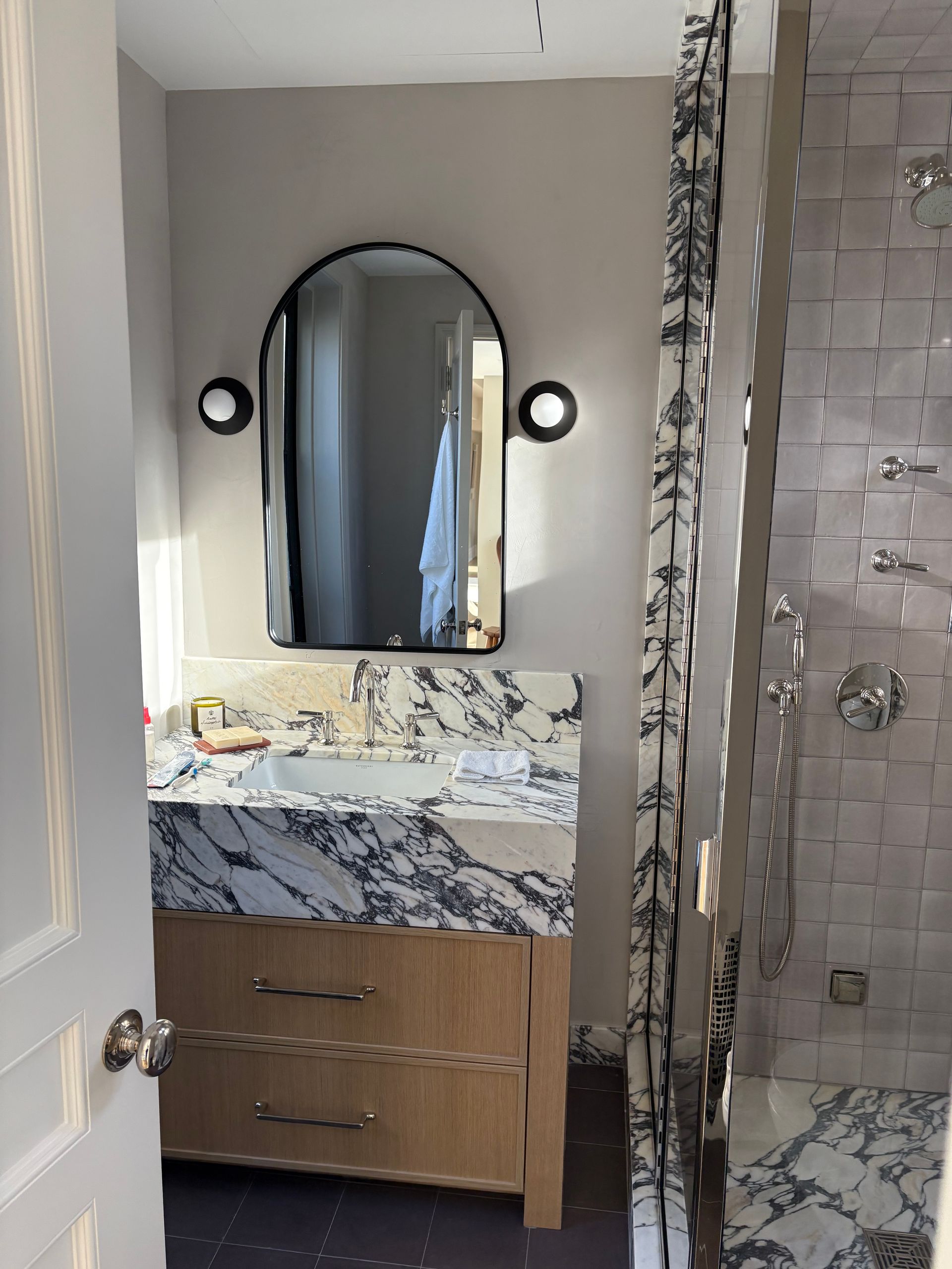 Bathroom with marble countertop, arched mirror, and wood vanity