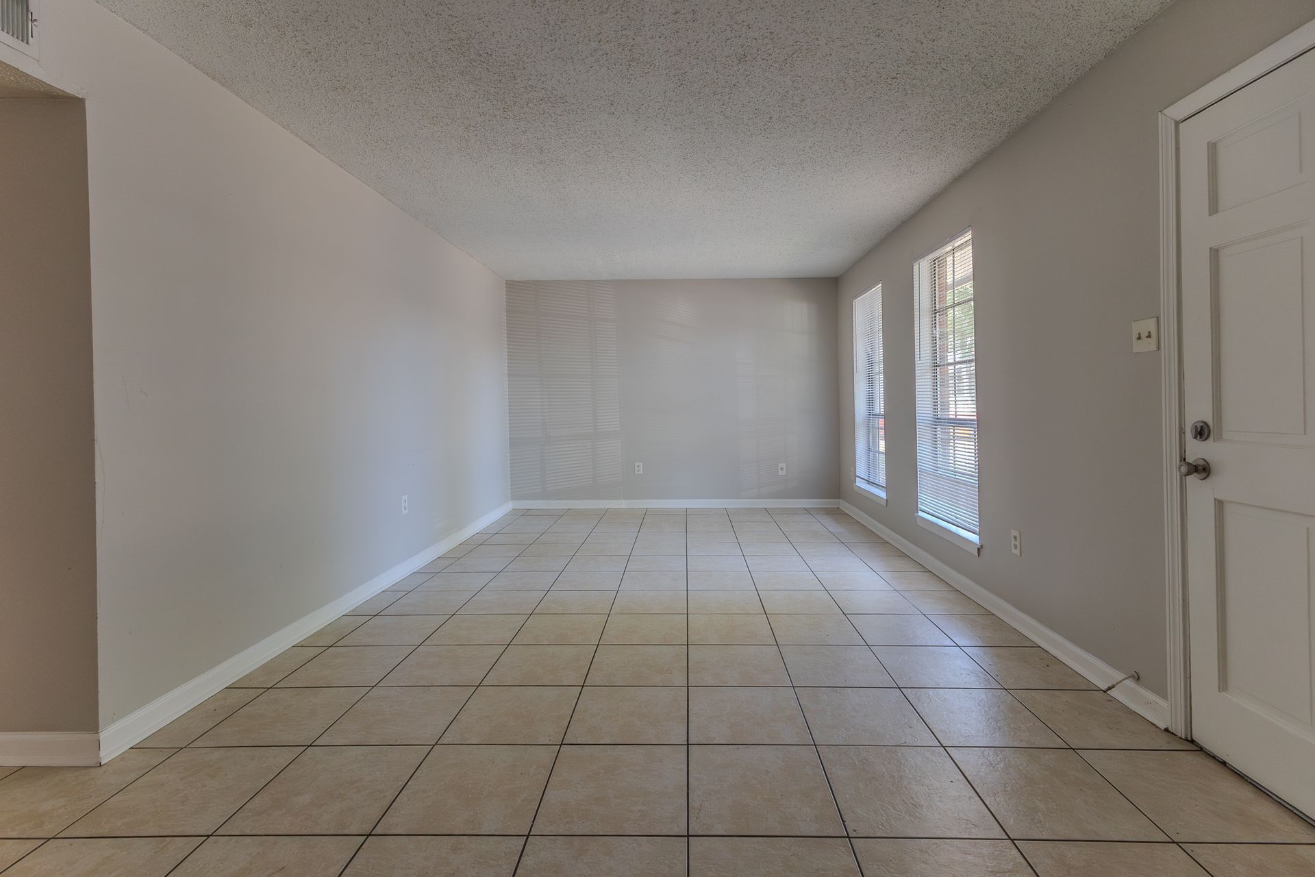 Empty room with beige tiled floor, light gray walls, and white door and trim.