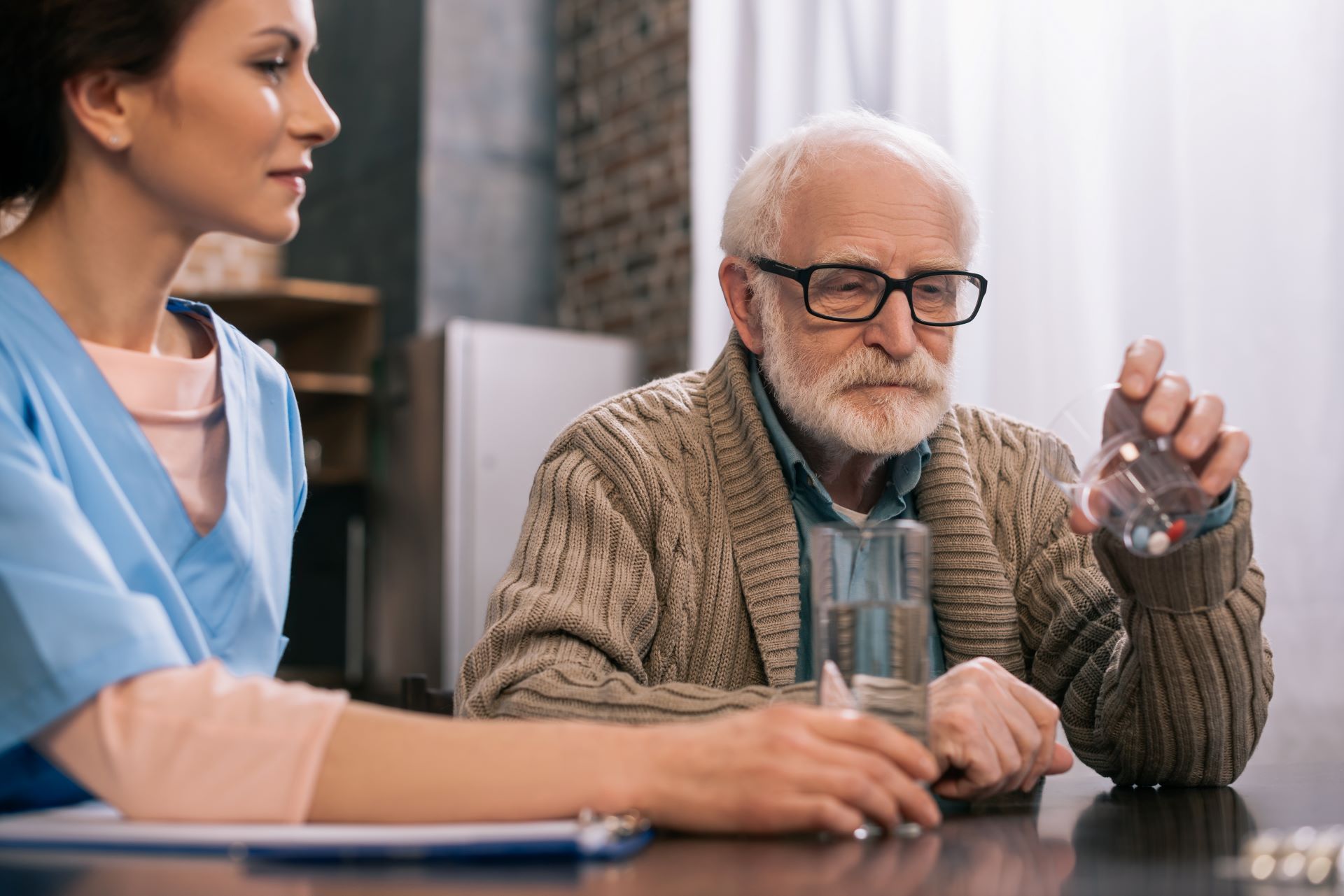 nurse sitting with senior man at table as he takes medications