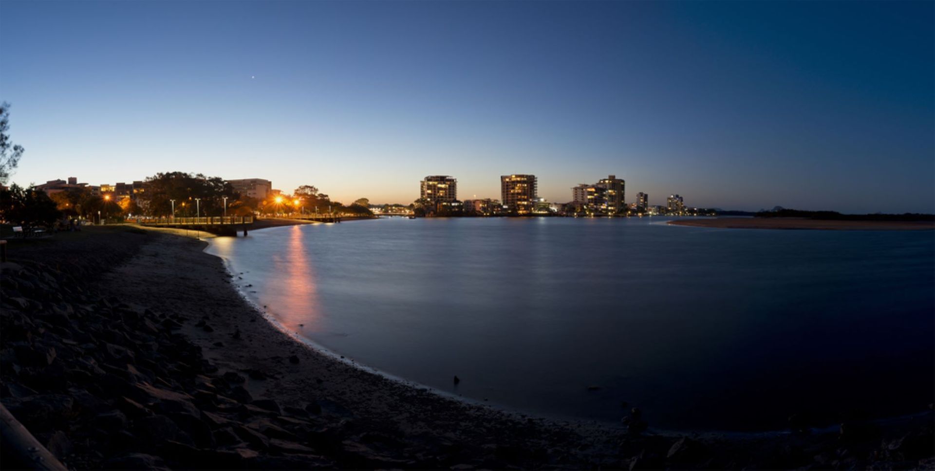A City Skyline is Reflected in the Water at Night — Aura Towing Service in Maroochydore, QLD