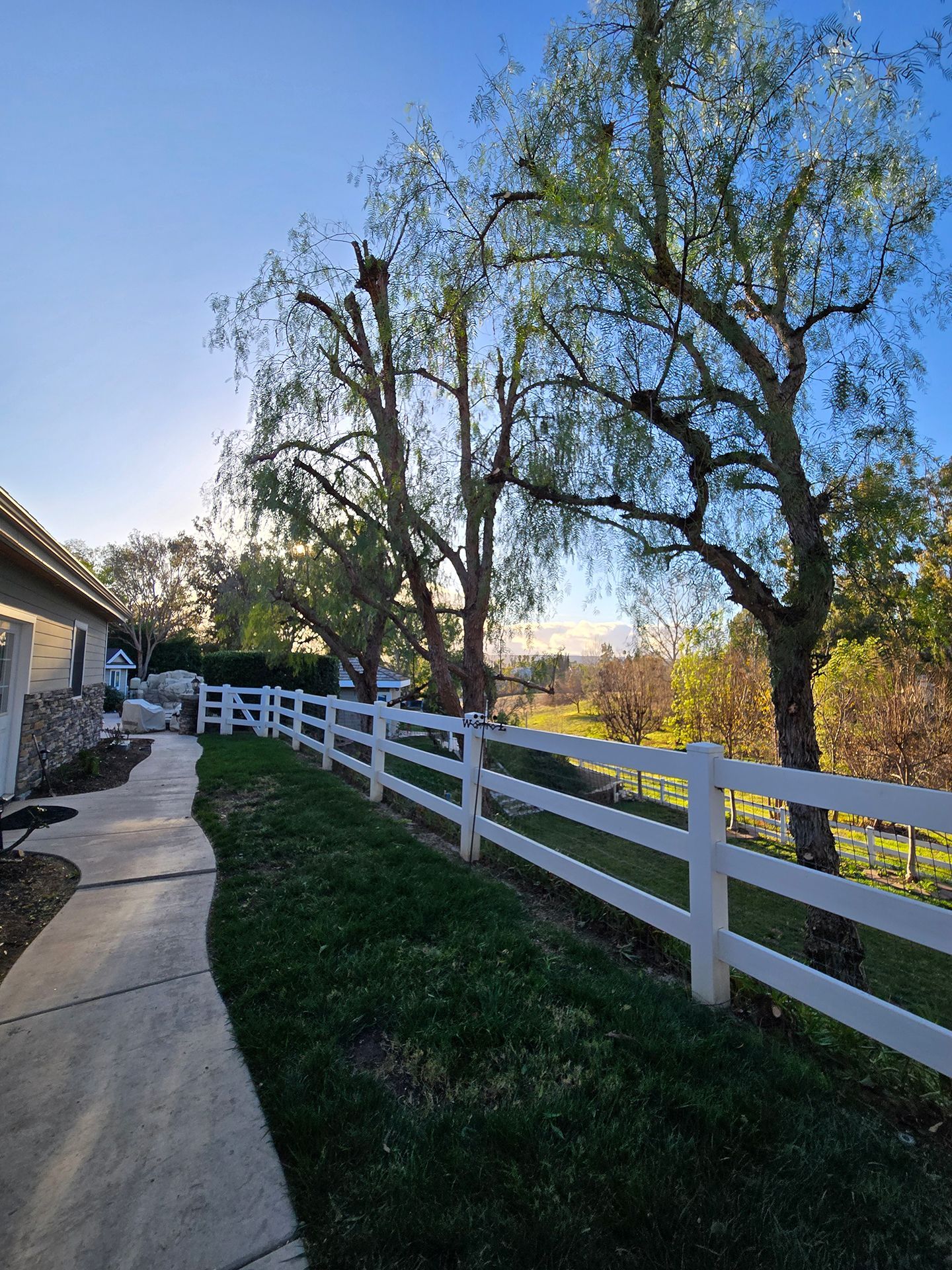 A white fence surrounds a lush green yard with trees in the background