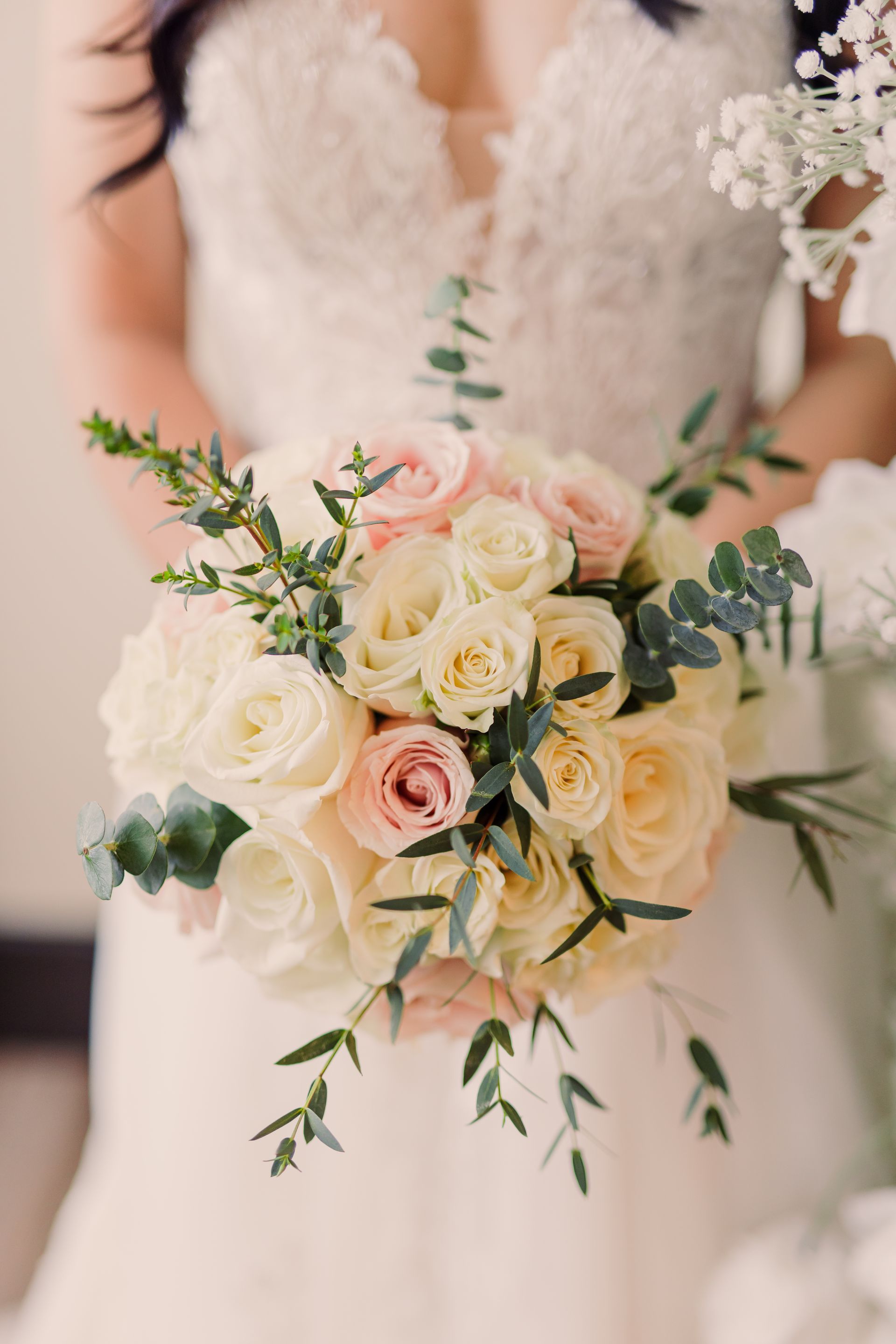 Bride holding a white and blush rose bouquet with greenery, wearing a lace wedding dress