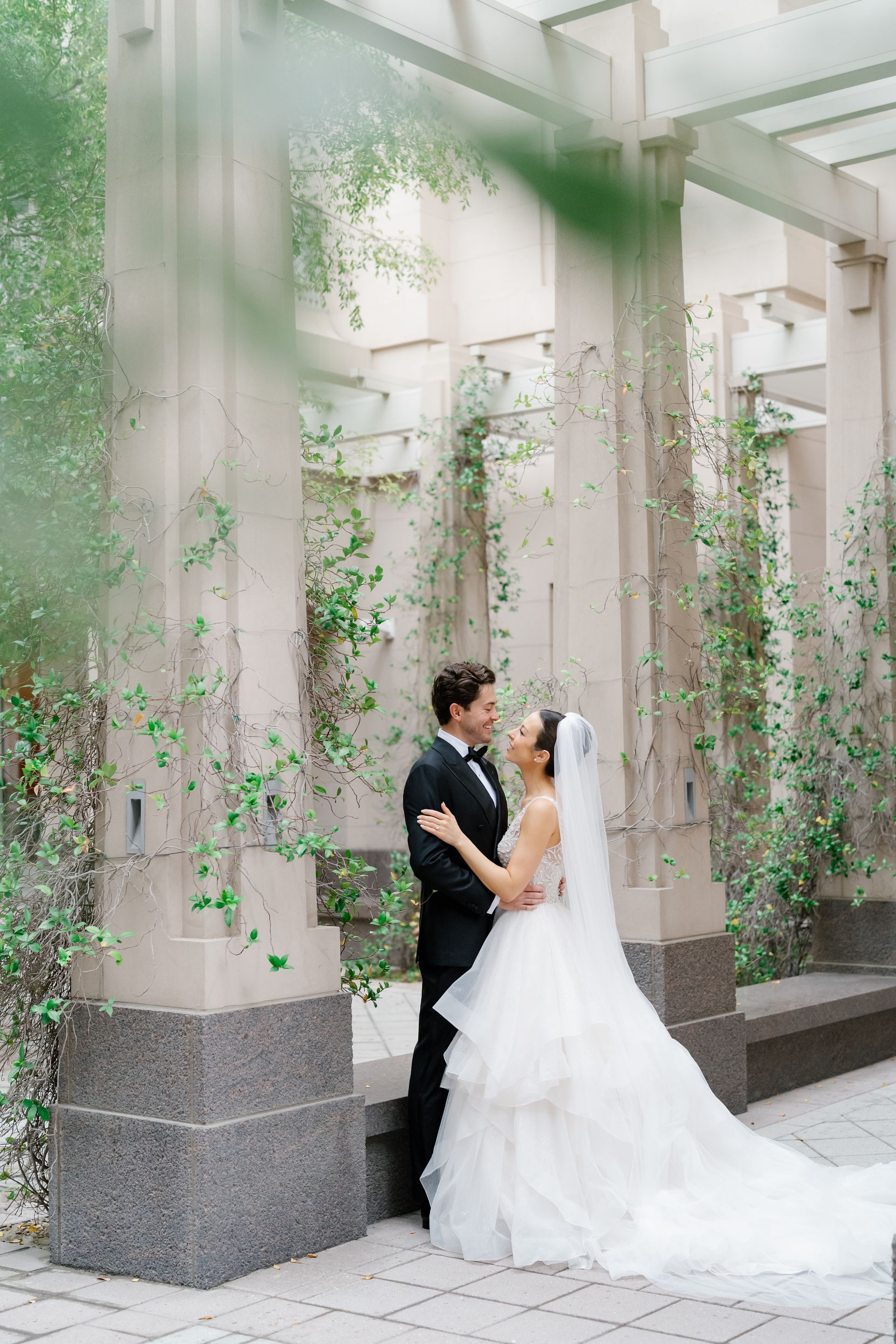 Bride and groom kissing under a vine-covered arch in an elegant courtyard
