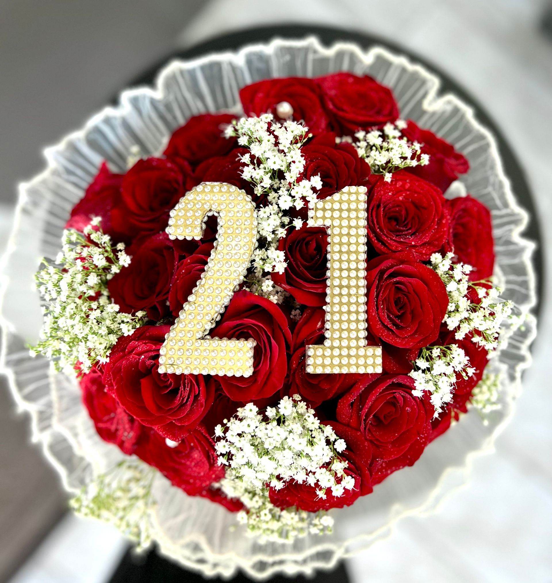Red rose bouquet with white flowers and gold “21” on a transparent wrapping