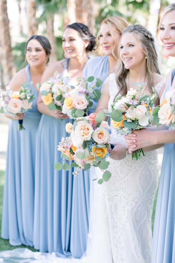 Bridesmaids in light blue dresses holding pastel bouquets at an outdoor wedding