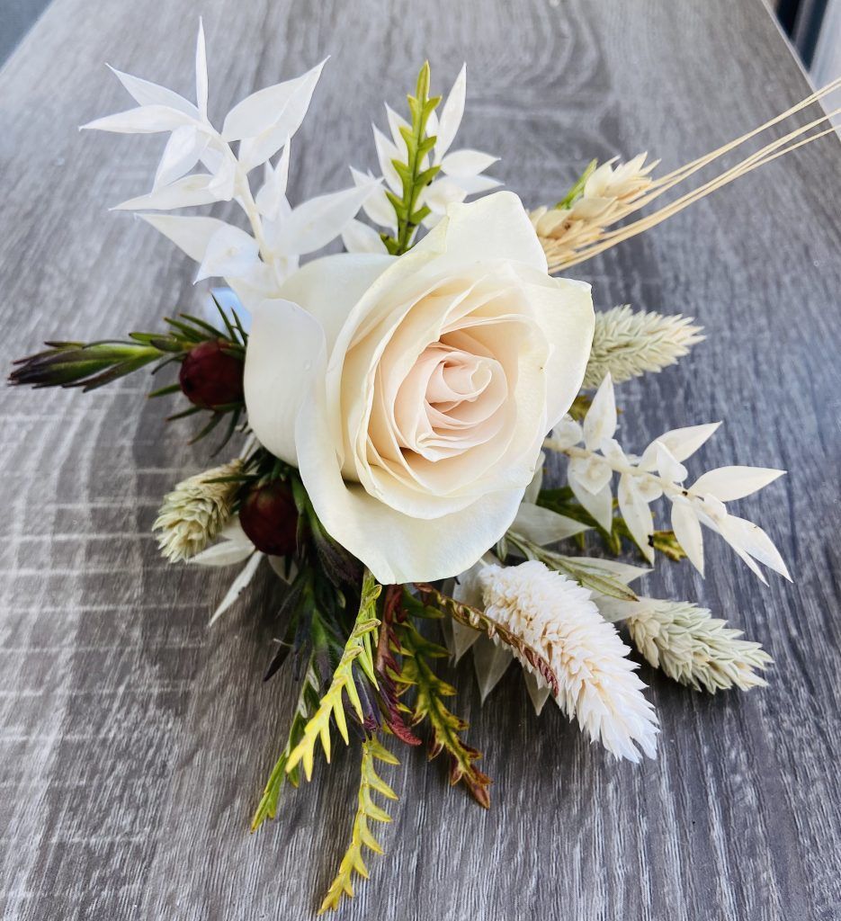 White rose floral arrangement with green and burgundy accents on a gray wooden surface