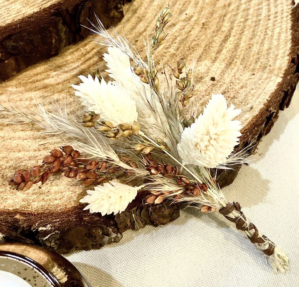 Rustic dried floral arrangement with white leaves and beige grasses on a wood slice backdrop