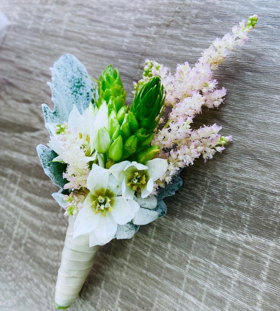 White and pastel floral boutonniere with green accents on a gray textured background