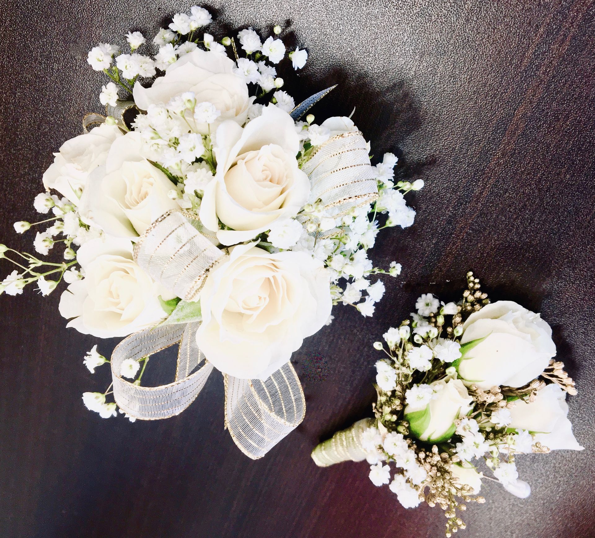 Two white rose bouquets with baby's breath and white ribbon on a dark background