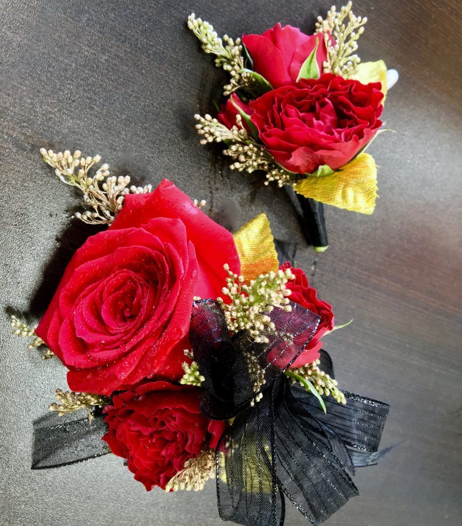 Two red rose boutonnieres with black ribbon on a dark surface