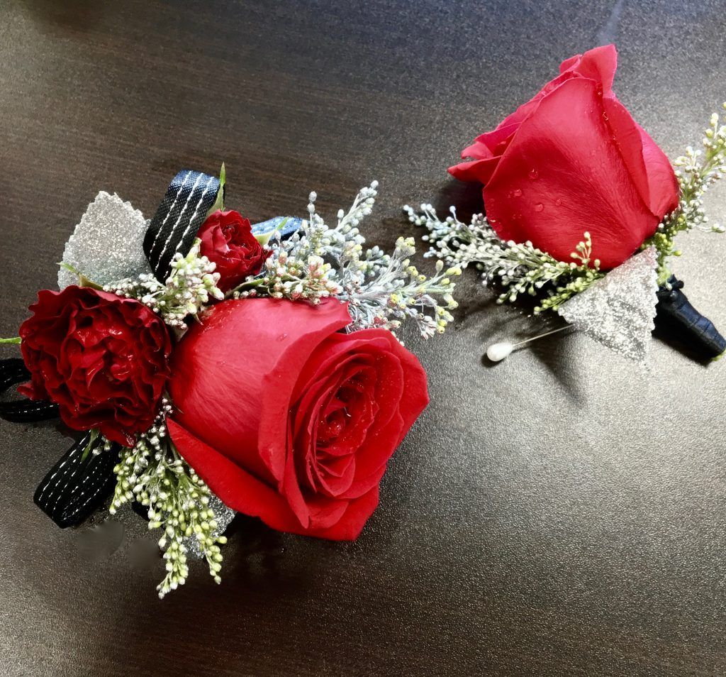 Two red rose boutonnieres with baby's breath and black ribbon on a dark surface
