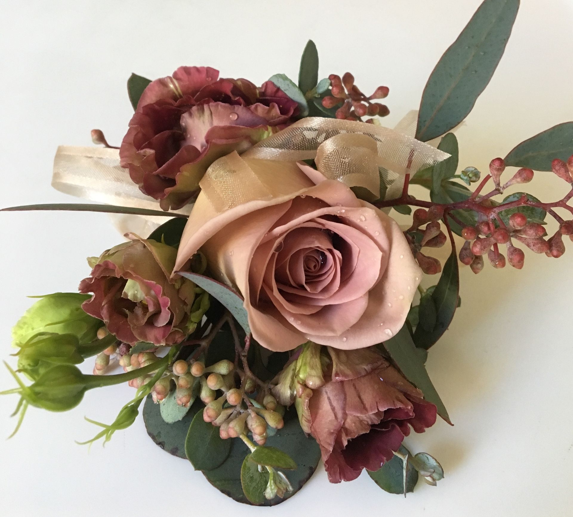 Dusty pink and burgundy artificial floral bouquet with green leaves on a white background