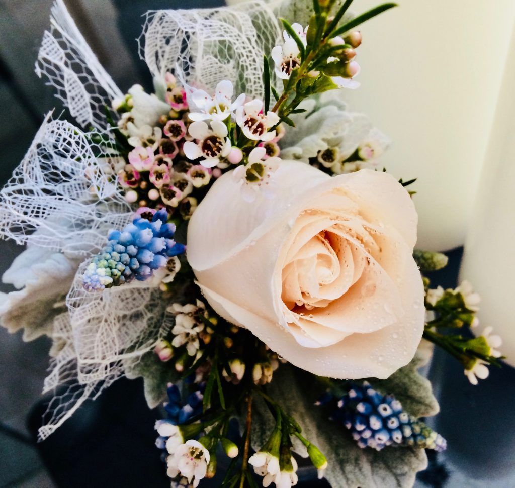 Cream rose bouquet with white lace, blue berries, and small pink flowers on a dark background
