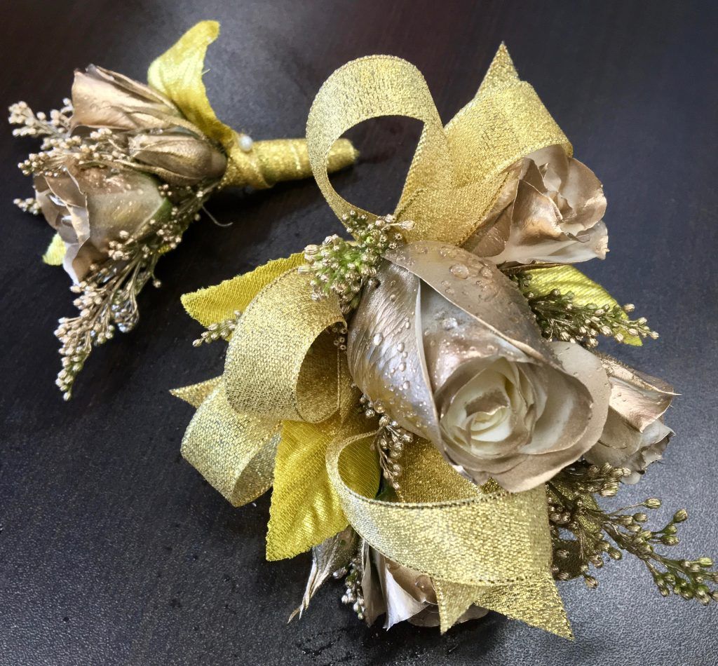 Gold and beige floral corsages with ribbon and metallic accents on a dark surface