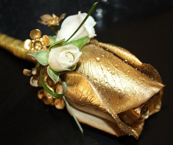 Gold satin wrist corsage with white roses and green accents on a black background