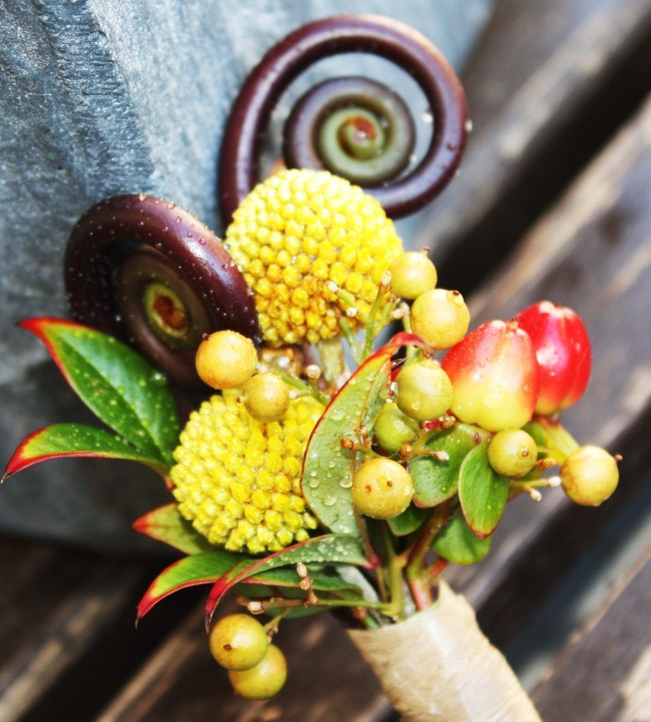 Close-up of a colorful bouquet with yellow berries, red fruit, and curled dark stems on wood background