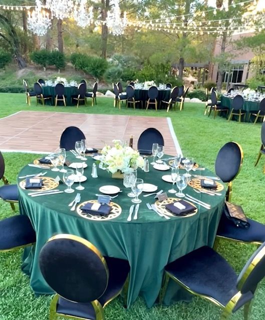 Round banquet table with dark green tablecloth and place settings in a garden under hanging string lights.