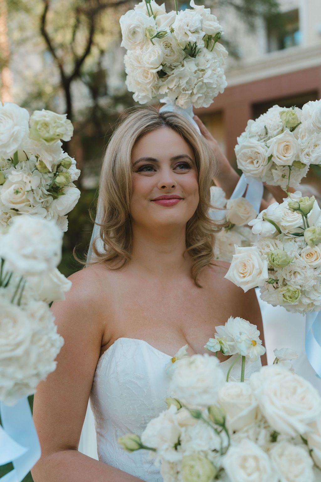 Bride holding white bouquet surrounded by white flowers at an outdoor wedding