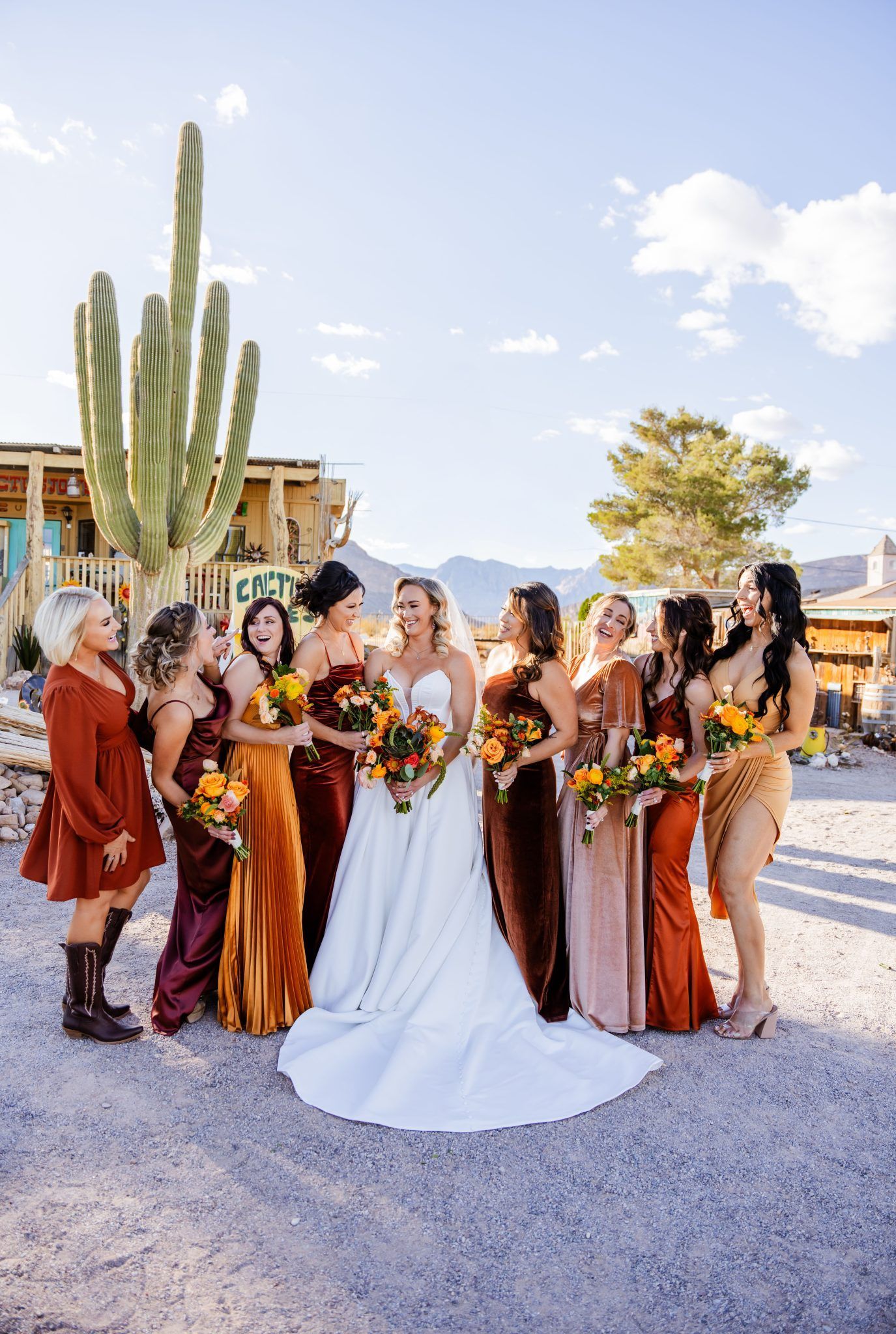 Bridal party posing outdoors in formal dresses, with the bride in white holding a bouquet.
