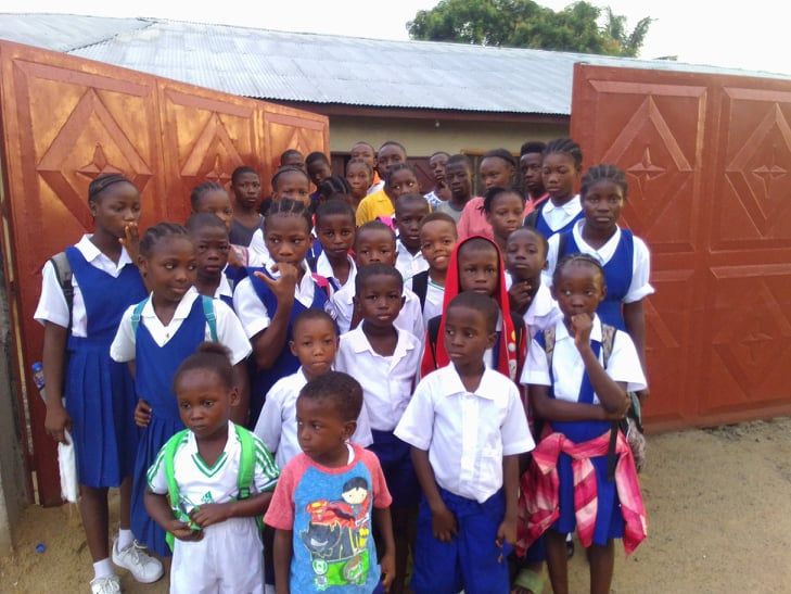 Group of schoolchildren in blue and white uniforms standing outside a school gate