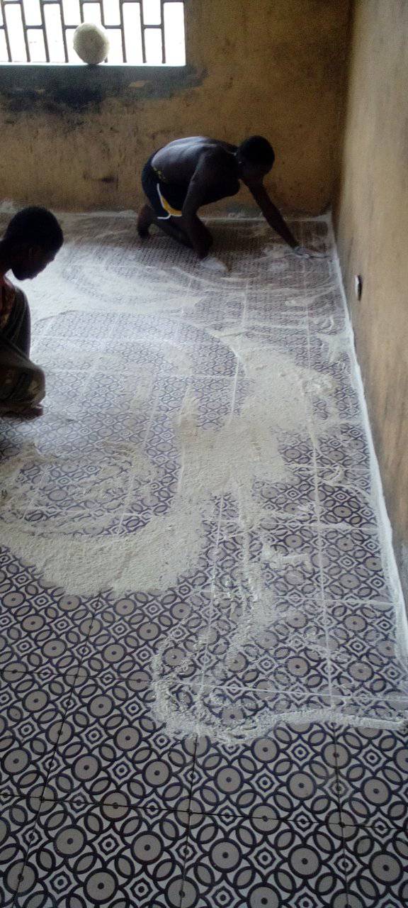 Two people cleaning a patterned floor in a bare room with barred windows.