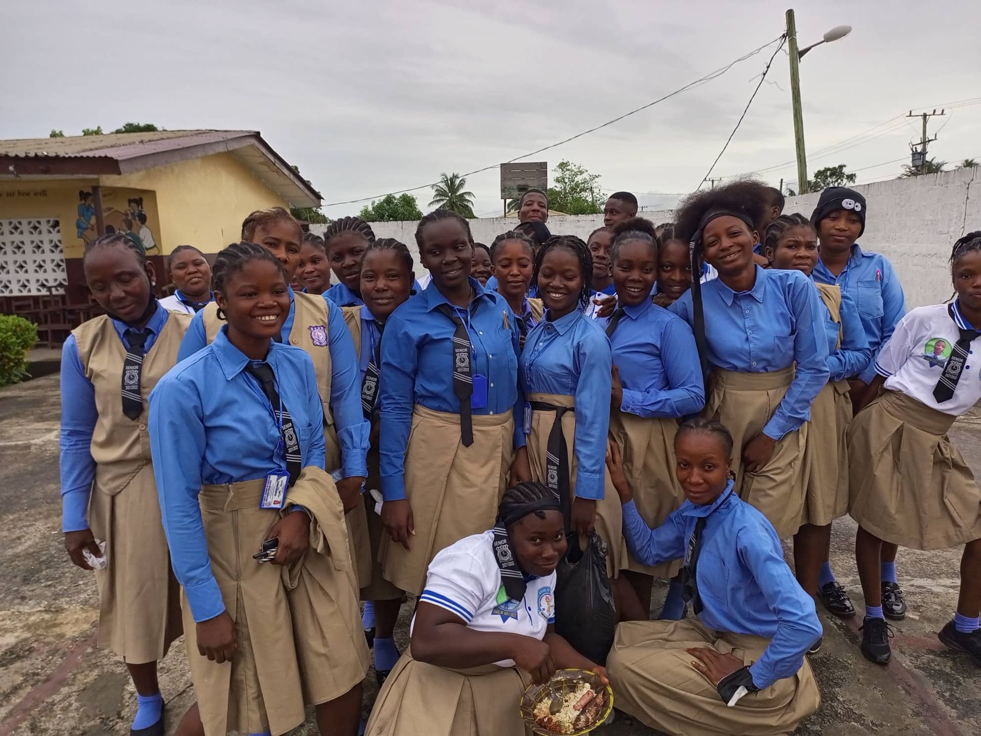 Group of students in blue shirts and tan skirts posing outdoors in a courtyard