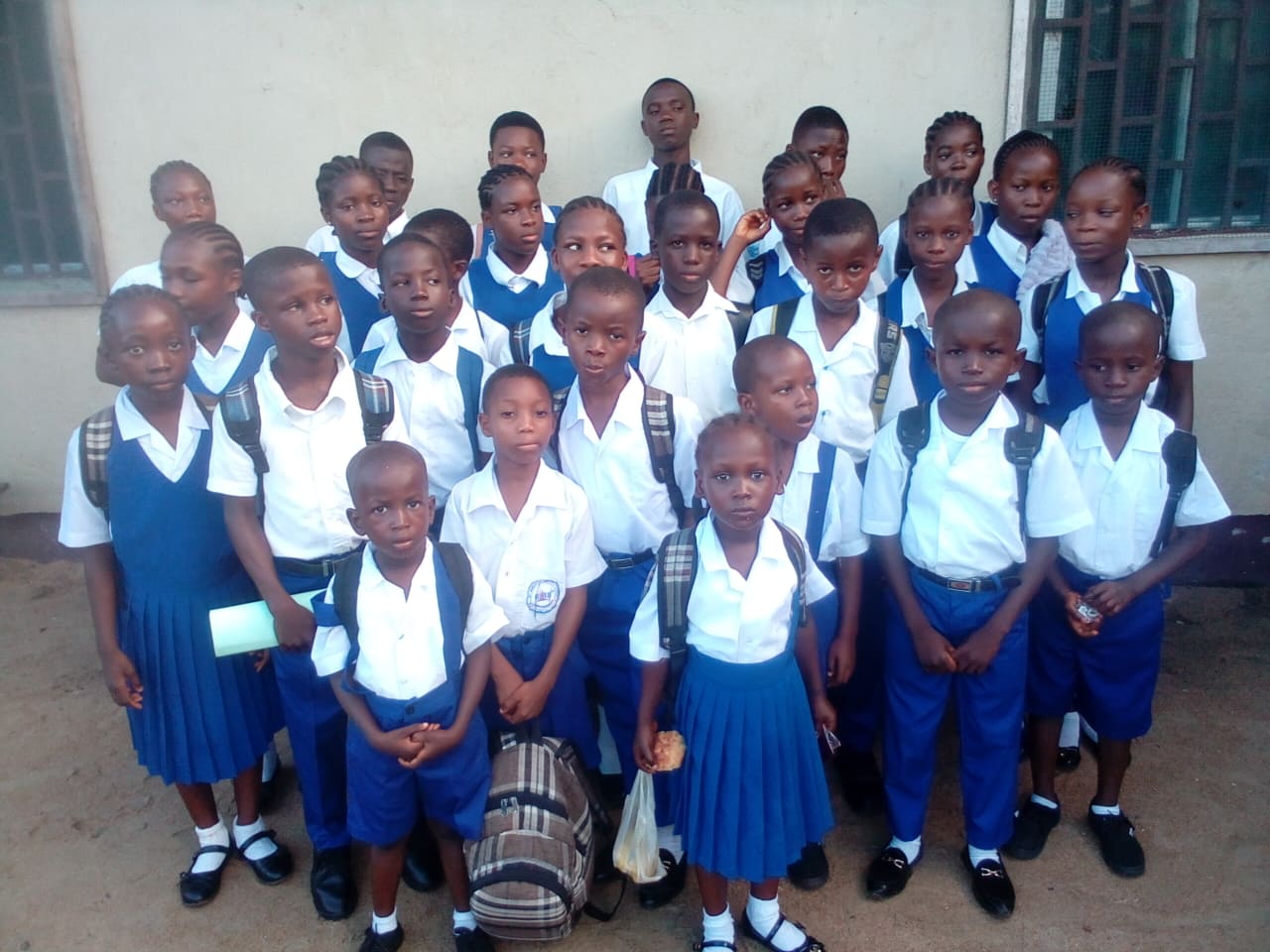 Group of schoolchildren in blue-and-white uniforms posing for a class photo indoors