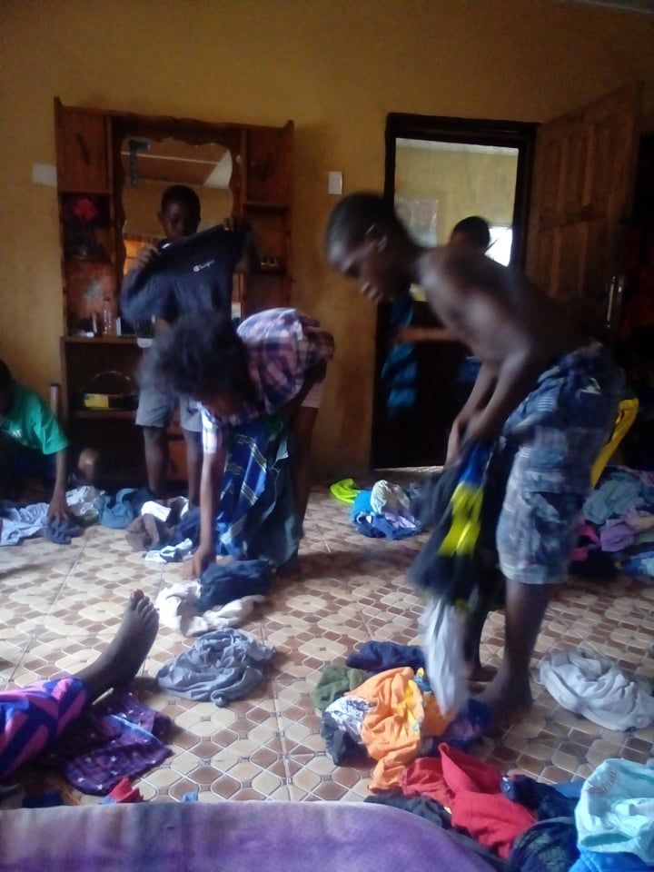 People packing clothes into bags in a cluttered room with patterned tile floor.