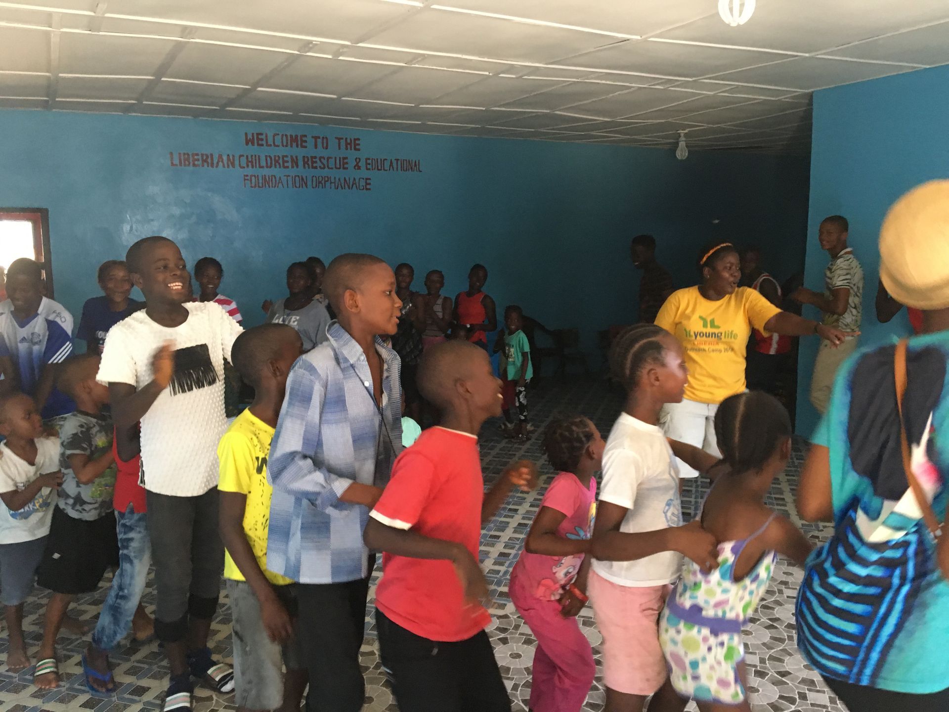 People dancing in a crowded indoor hall with blue walls and a wooden floor