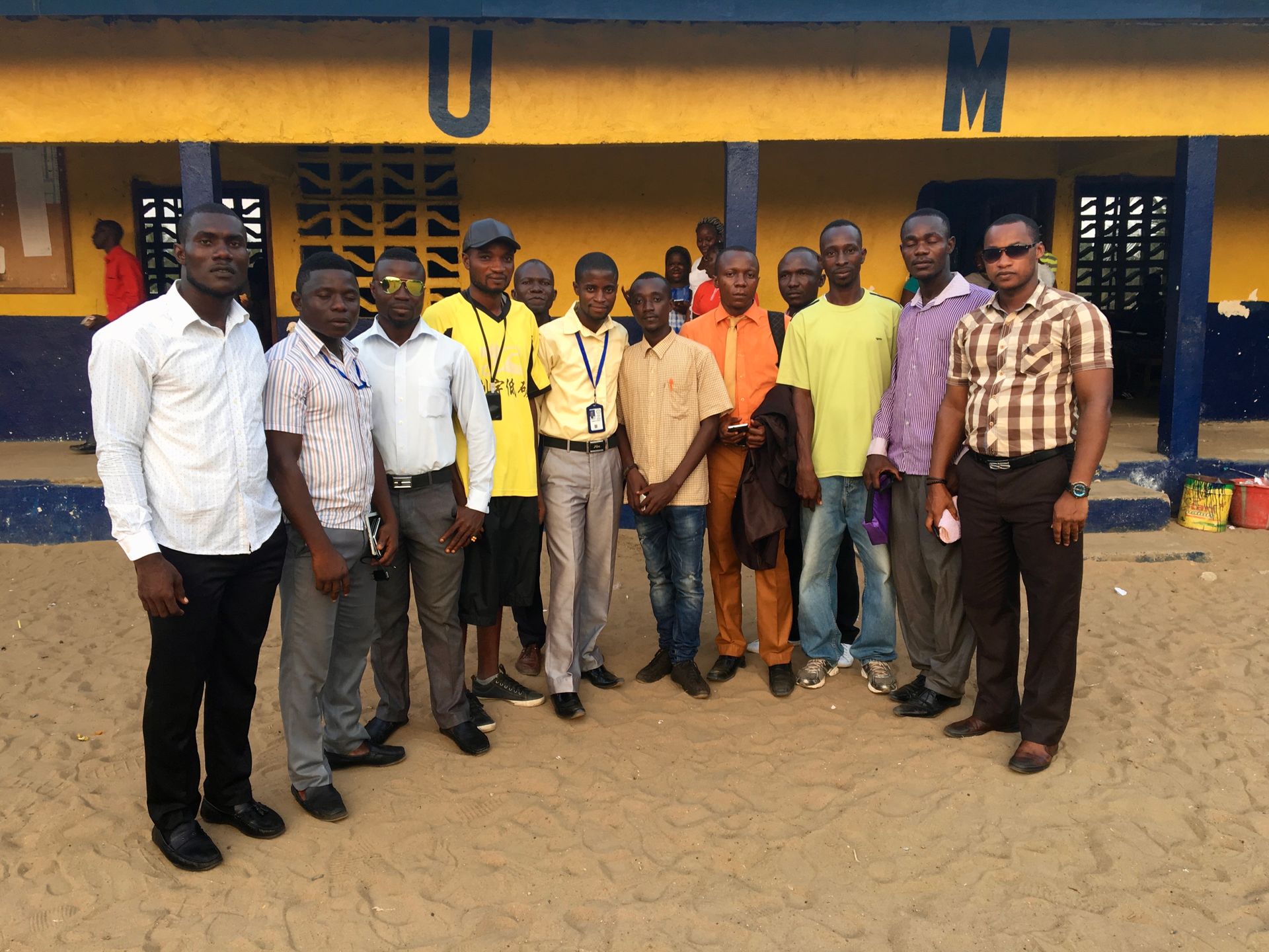 Group of people standing outside a yellow-and-blue building, posing for a photo.